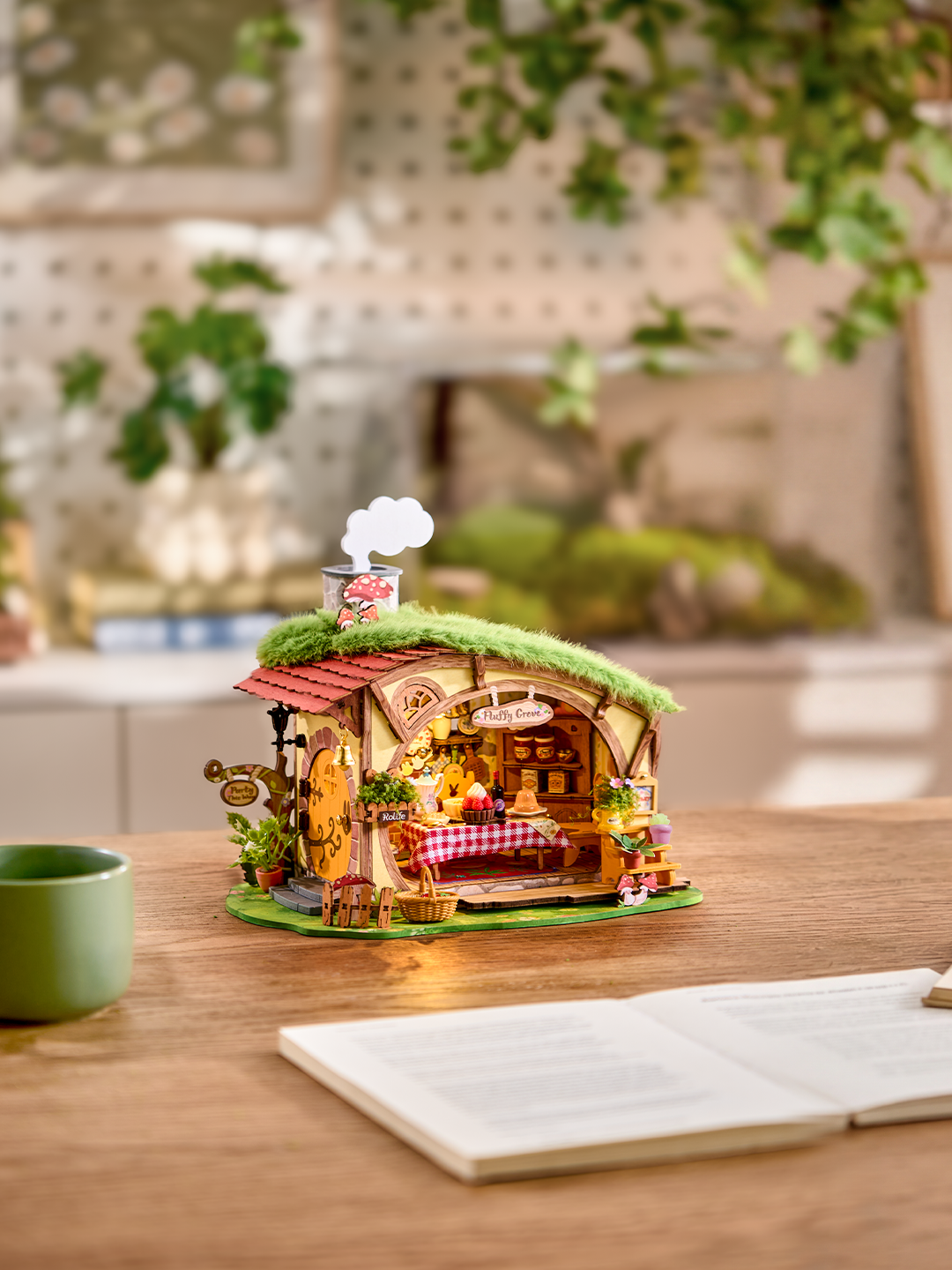 Completed Rolife Fluffy Grove DG184 miniature house on a wooden desk beside a mug and open notebook
