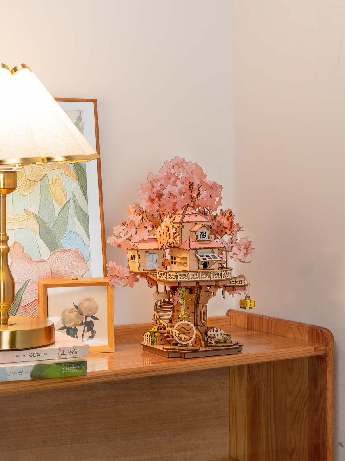 Rolife Sakura Tree House TGS04 wooden 3D puzzle displayed on a cabinet beside a lamp and framed art