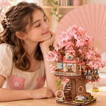 Girl admiring the assembled Rolife Sakura Tree House TGS04, with pink blossoms, wooden stairs and a hanging basket.