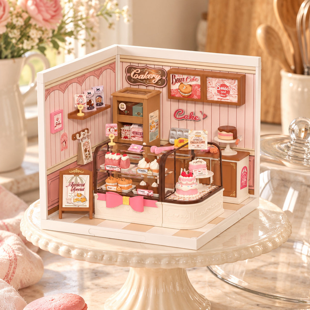 Assembled Rolife Tasty Cake Shop DW019B miniature bakery displayed on a glass cake stand with pink table linens.